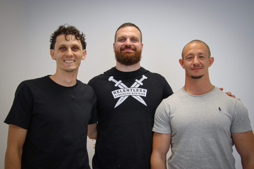 leo-paul-sapet-preparateur-mental-podcast-powerlifting-forceathletique-relentless.webp Léo-Paul avec deux joueurs du FCBJ devant le mur média du club avec les logos sponsors